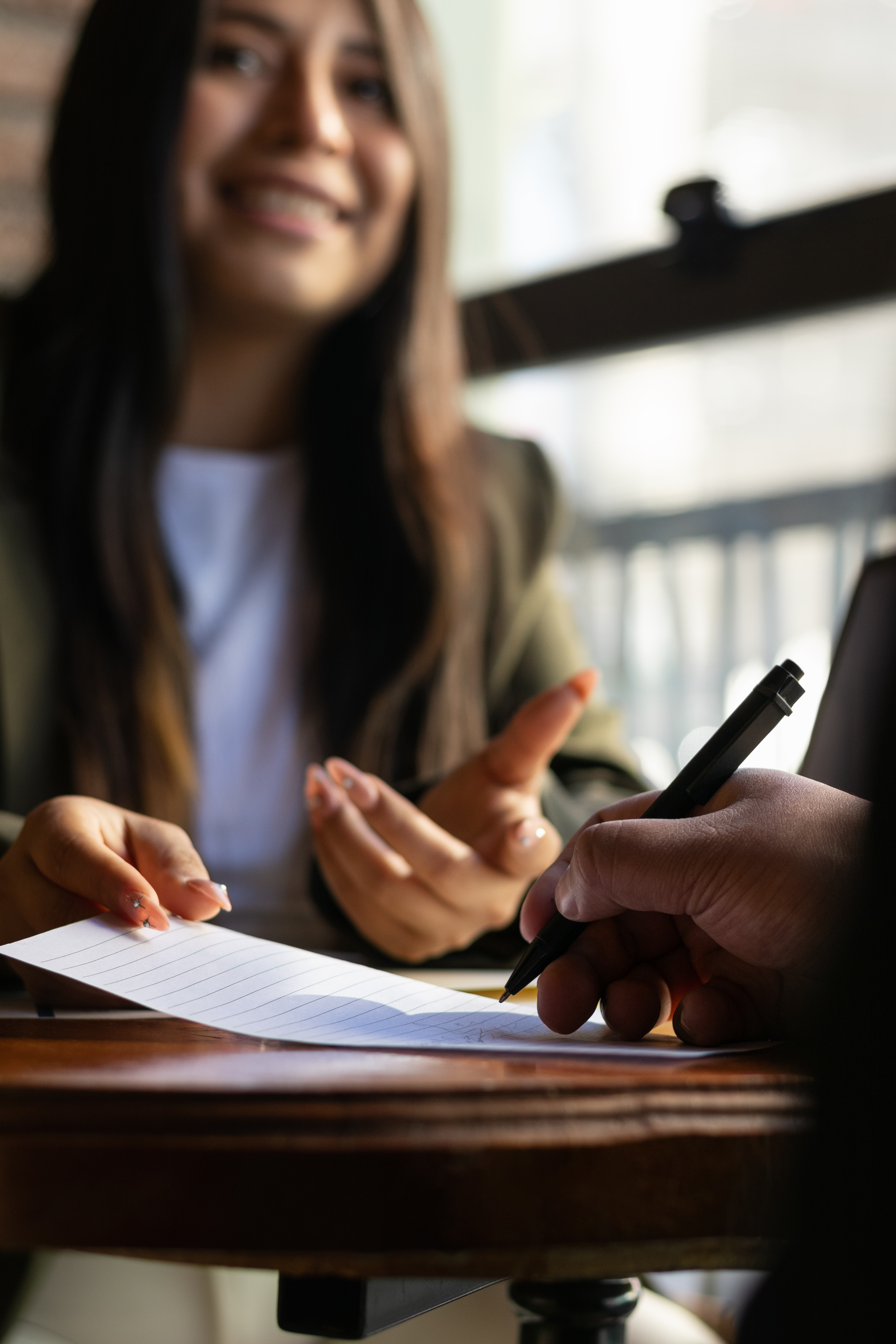 Close-up with copy space of a man's hand signing a legal document with a pen while a formal woman in a suit is smiling in her office creating a professional atmosphere.