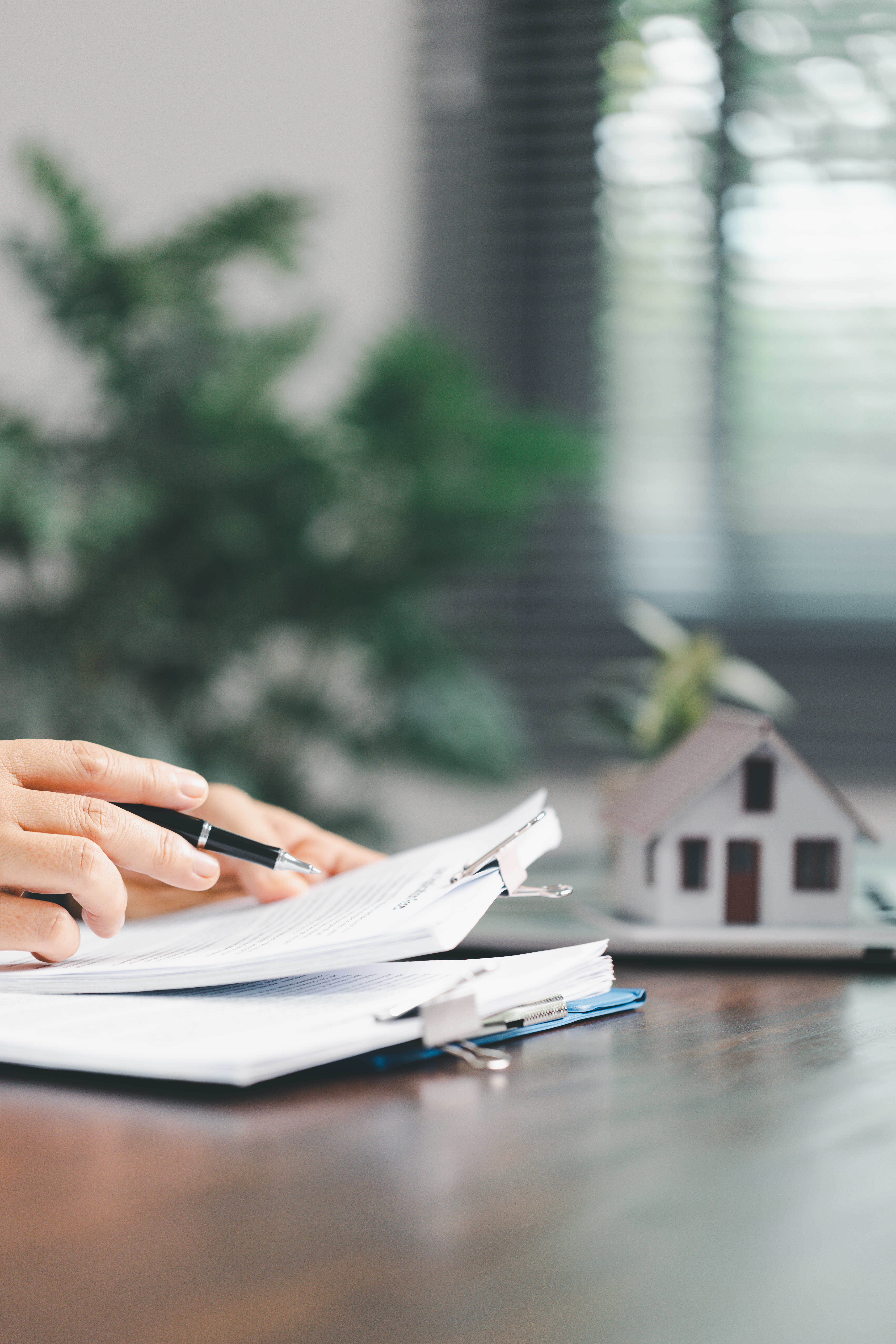 Real estate agent and customer are discussing contract to buy house, with house model in background symbolizing real estate, insurance, and loan arrangements involved in process.